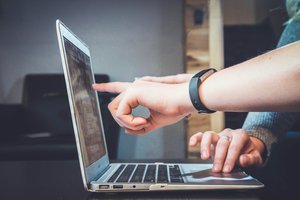 Une personne montre un ordinateur portable avec sa main.