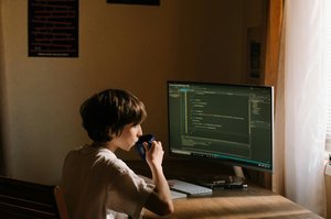 Développeur buvant dans une tasse devant son écran avec du code affiché