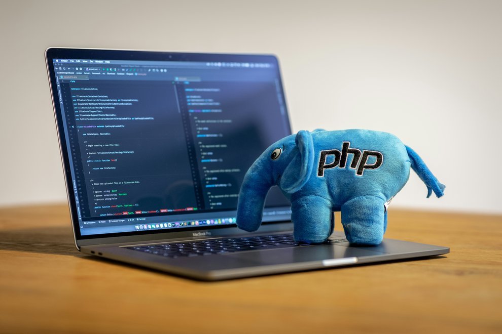 Ordinateur portable posé sur une table avec du code PHP à l'écran et la mascotte de PHP posée sur le clavier